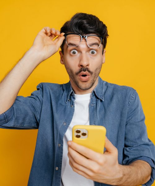 Amazed,Charismatic,Unshaven,Caucasian,Guy,Holding,Smartphone,In,His,Hand,
